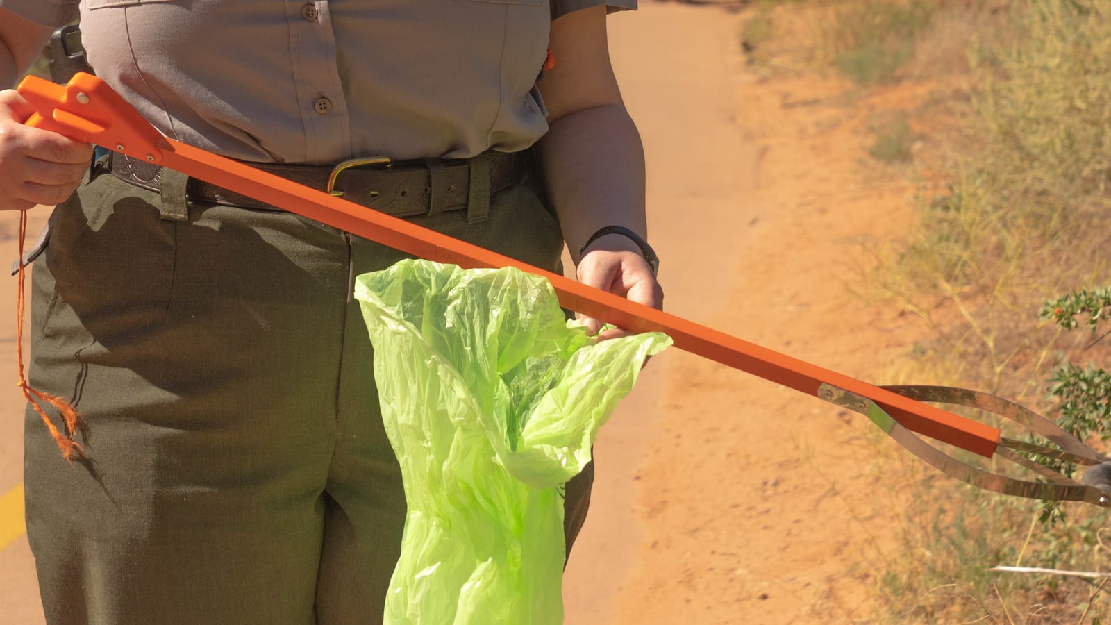 A litter grabber and collection bag in a volunteer's hands