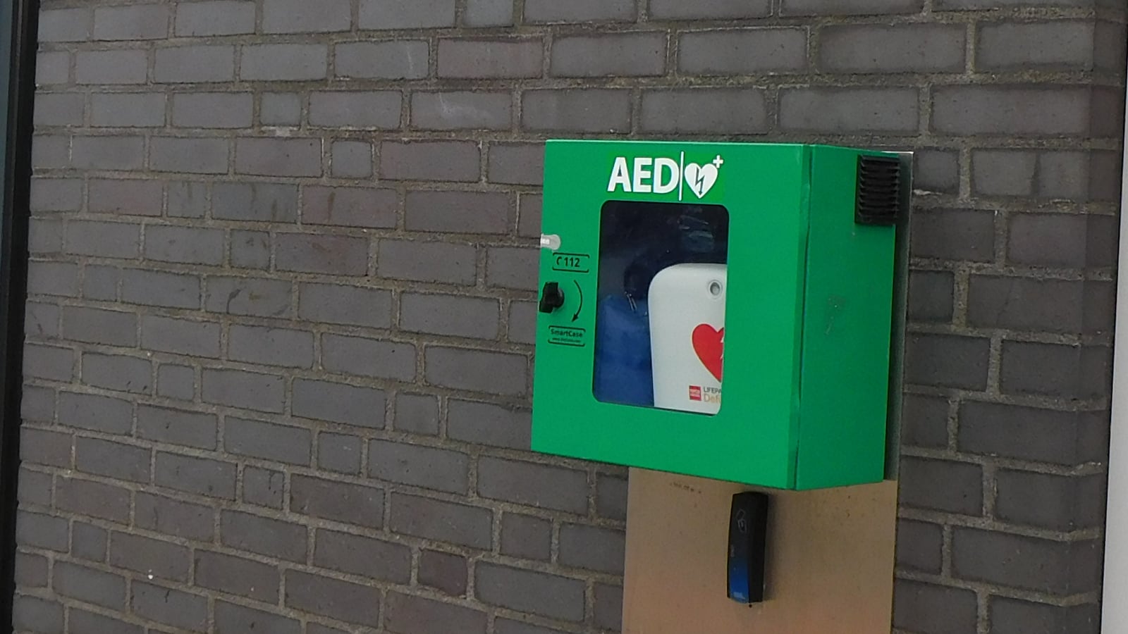A public defibrillator cabinet mounted on a brick wall