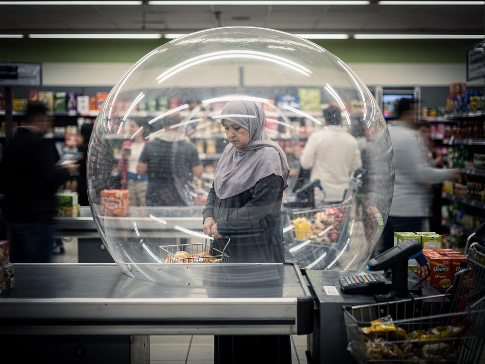 A generated image: a woman shopping, enclosed alone inside a transparent bubble in a busy supermarket